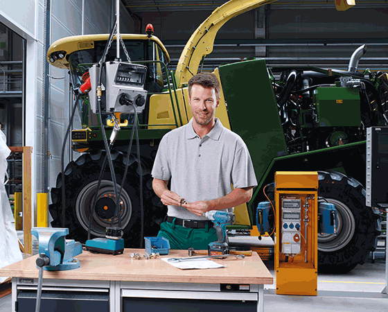 A man stands in front of a workbench in front of a yellow MENNEKES power distributor and a tractor
